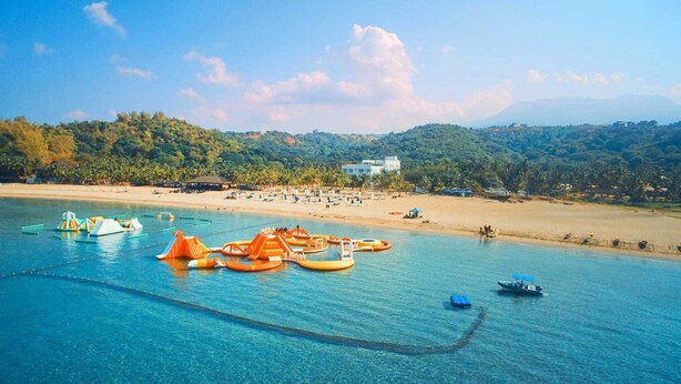 A beach with clear blue water, orange floating structures, and a sandy shore with umbrellas and beach chairs. - Aqua Fun Hotel (Mariveles)