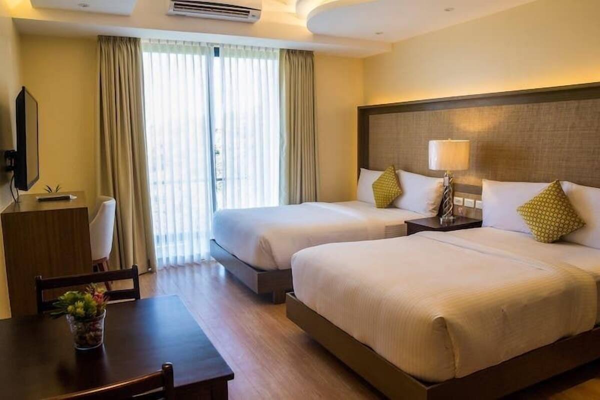 A hotel room with two beds, a desk, a chair, a TV, and a window with curtains.