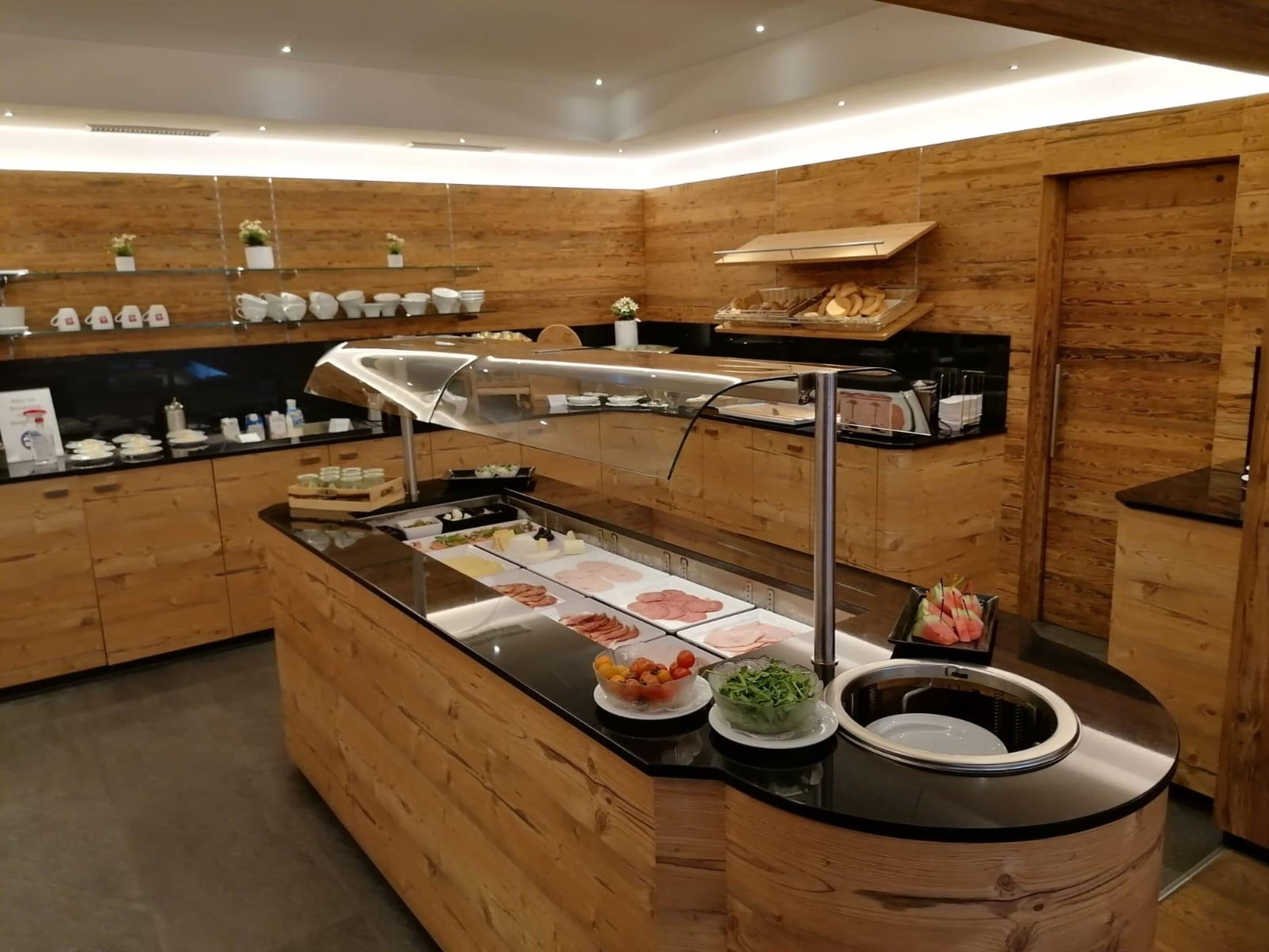 Un área de cocina moderna con una isla central que exhibe diversos alimentos, paneles de madera y un lavamanos de acero inoxidable.