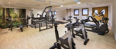 Un gimnasio con diversos equipos de ejercicio, suelo de madera y ventanas grandes.