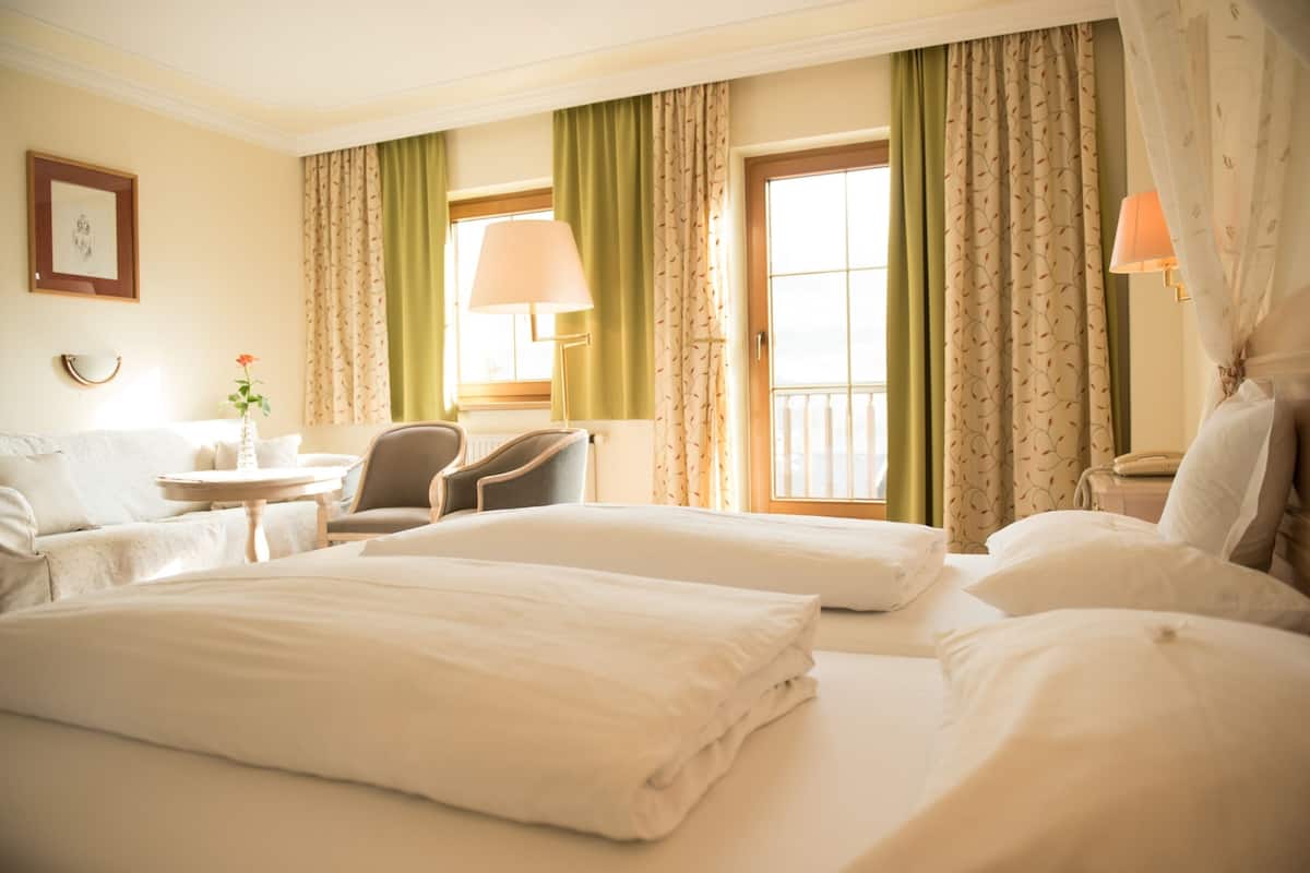 A hotel room with two beds, a chair, a table with a lamp, and a window with curtains.