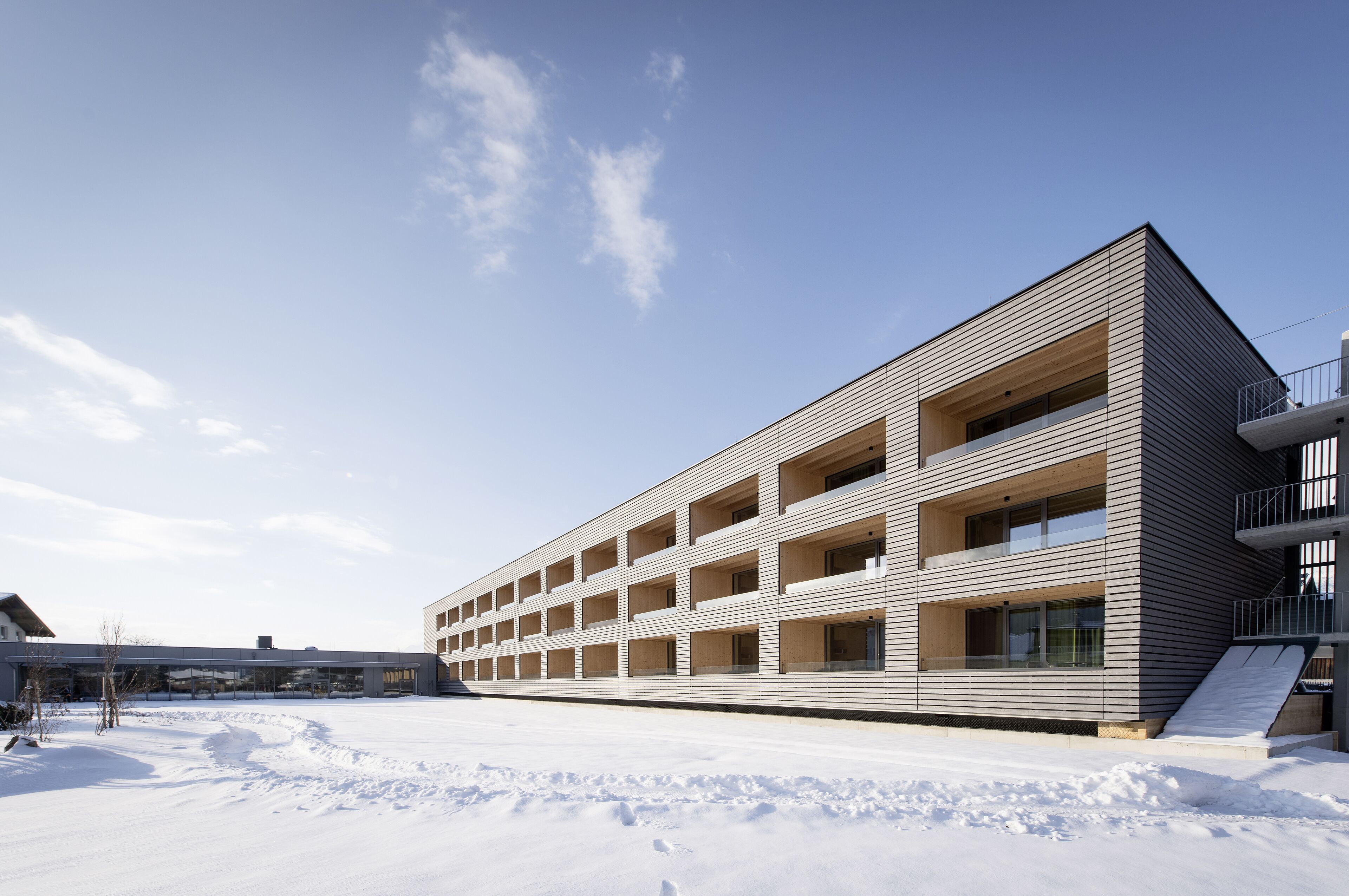 A modern multi-story building with a flat roof and a series of balconies.