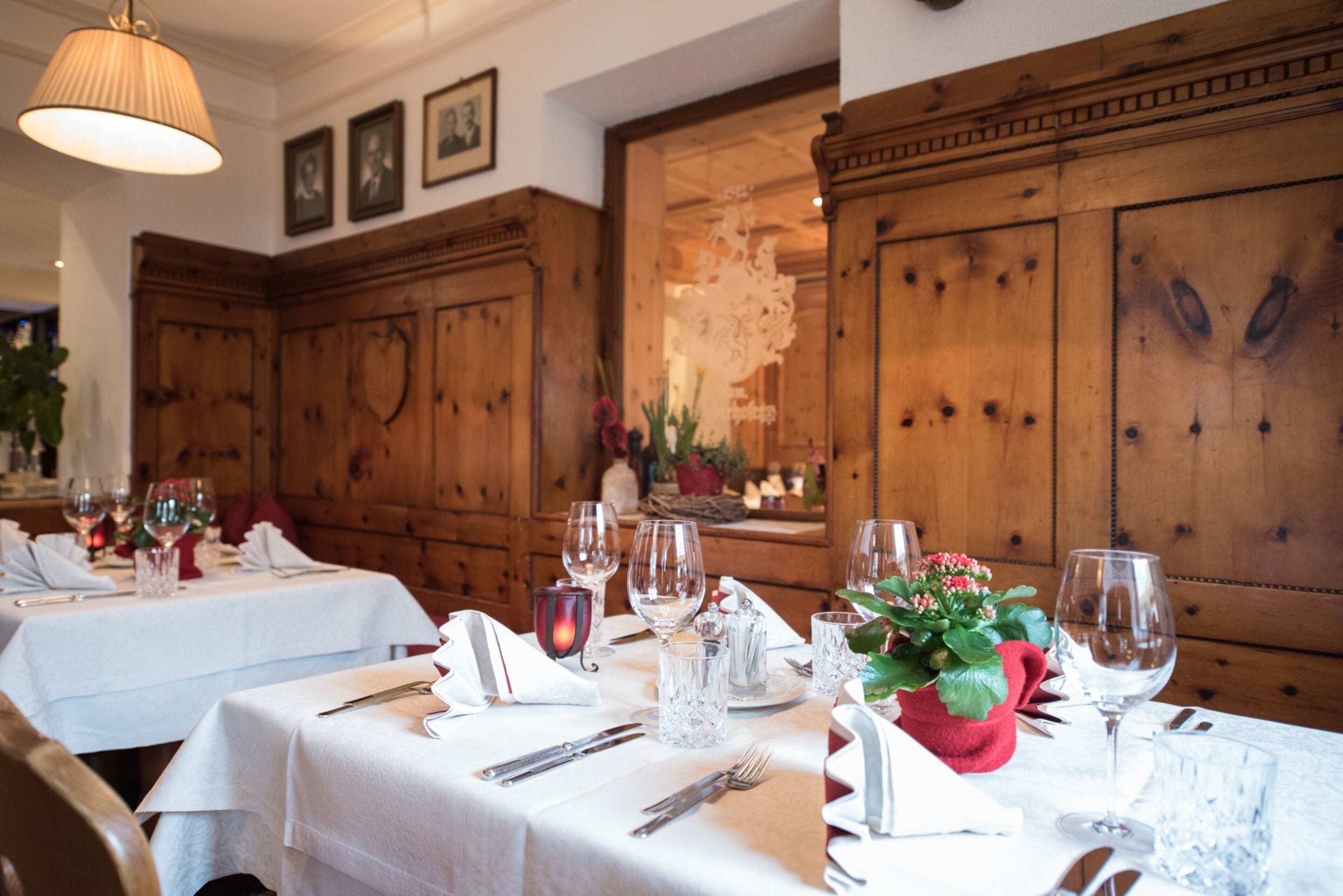 Un comedor con paneles de madera, manteles blancos y mesas ordenadas con copas de vino, cubiertos y una planta en maceta.