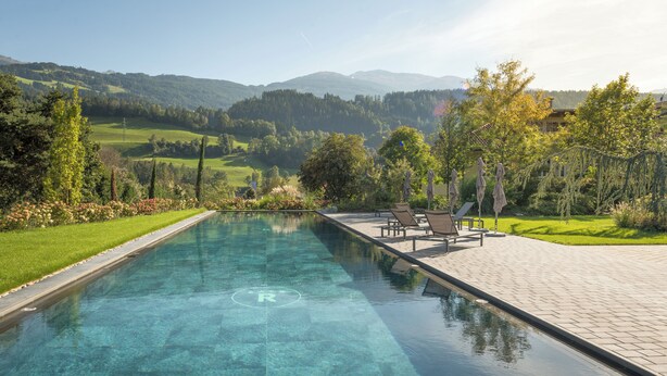 Une piscine aux eaux cristallines offrant une vue sur les montagnes, une terrasse avec des chaises et une pelouse bien entretenue.