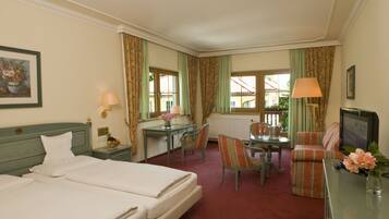 Habitación de hotel con cama, escritorio, silla, sofá, televisor y ventana con cortinas.