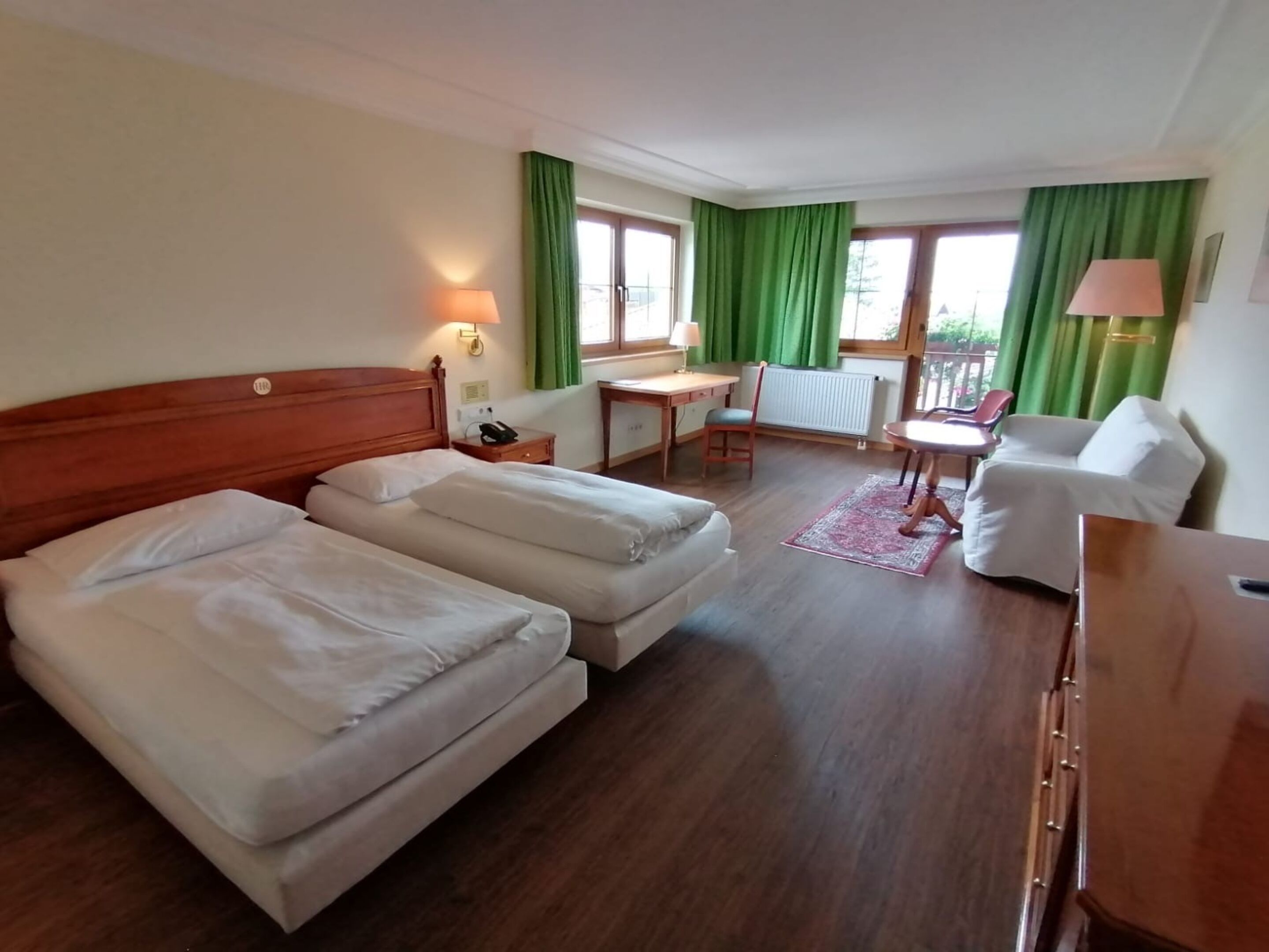 A hotel room with two beds, a desk, a chair, and a sofa.