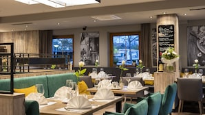 Un restaurant avec des sièges recouverts d’un tissu vert, des tables en bois et un menu écrit à la craie sur un tableau noir.