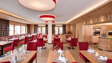 Een modern restaurant met rode stoelen en houten tafels, met een centrale kolom en grote rode hanglampen.