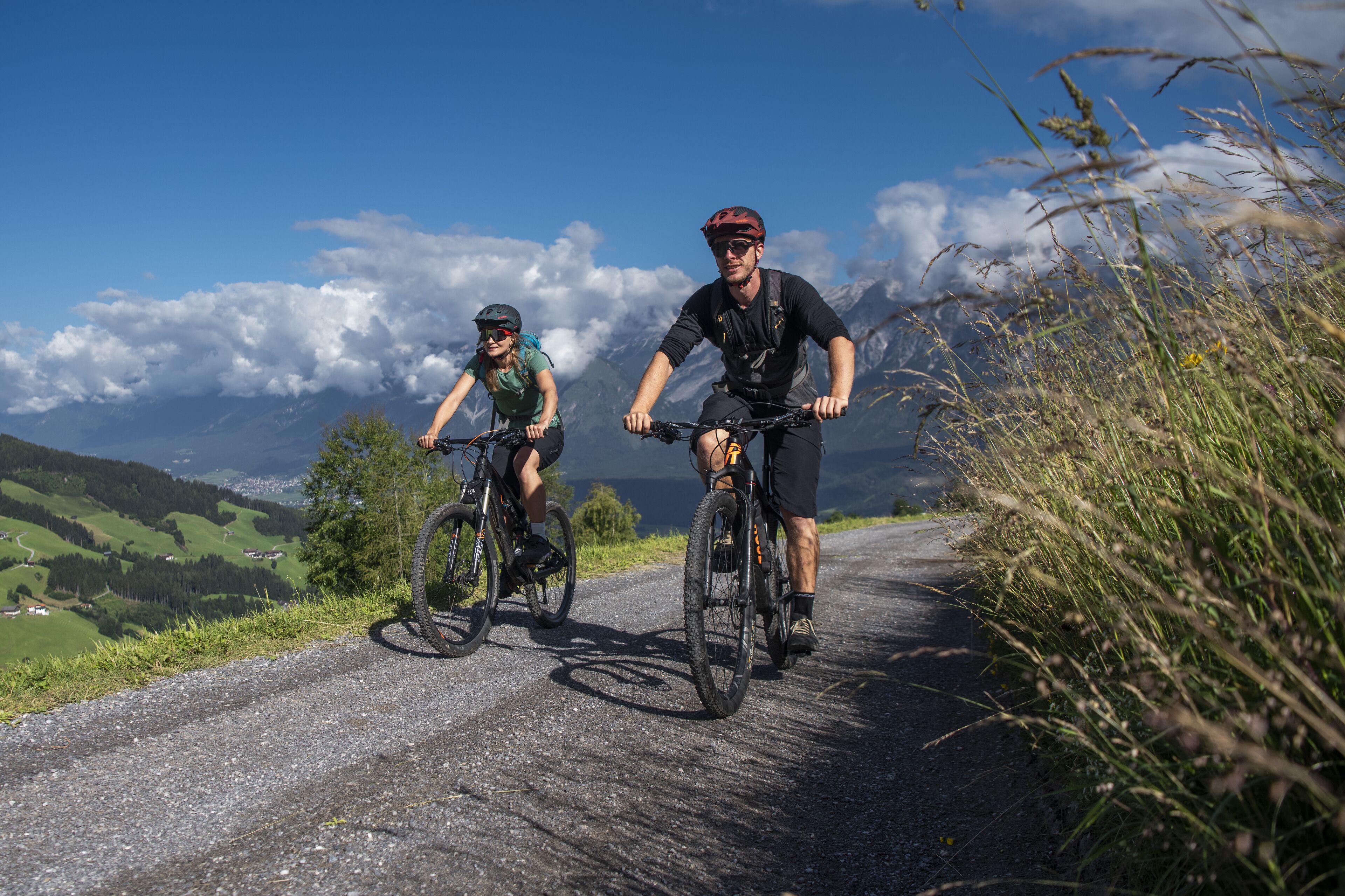 Two cyclists on a gravel road with a mountainous landscape in the background.