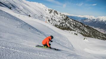 Ein Skifahrer auf einem verschneiten Hang unter blauem Himmel mit fernen Bergen im Hintergrund.