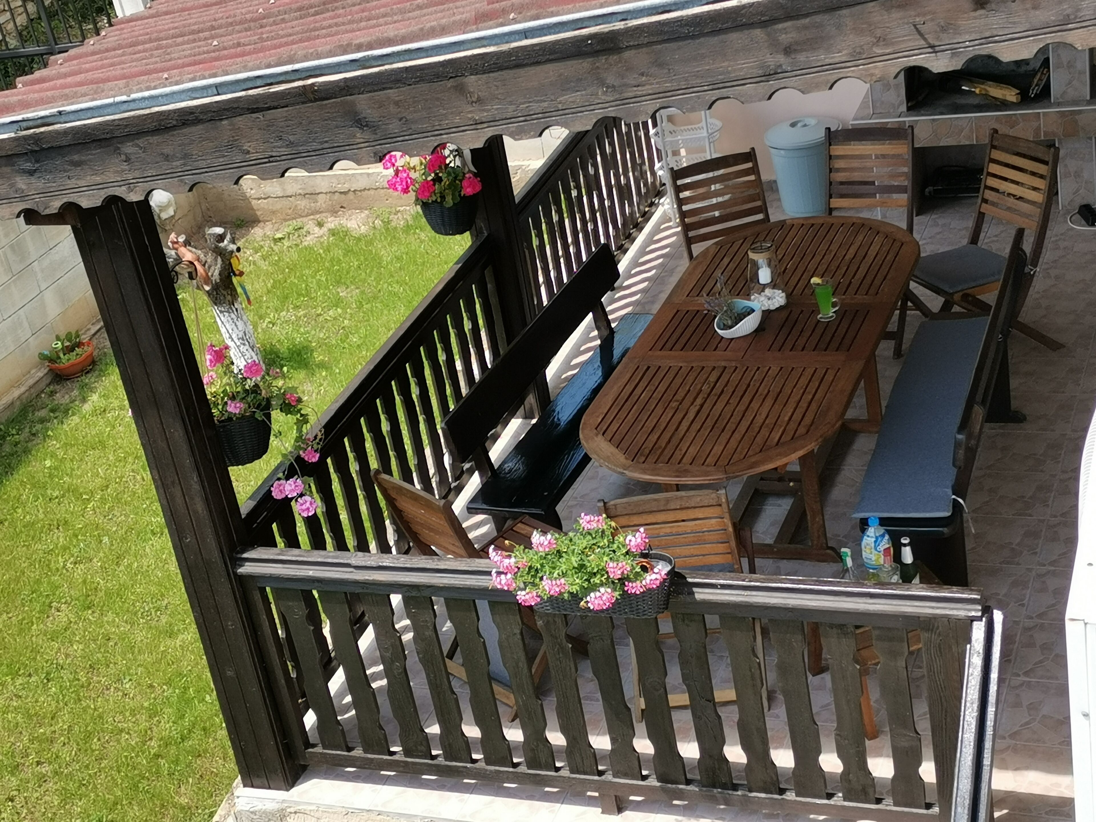 Eine Terrasse im Freien mit einem Holztisch, Stühlen, einer Bank und einem hängenden Blumenkorb.