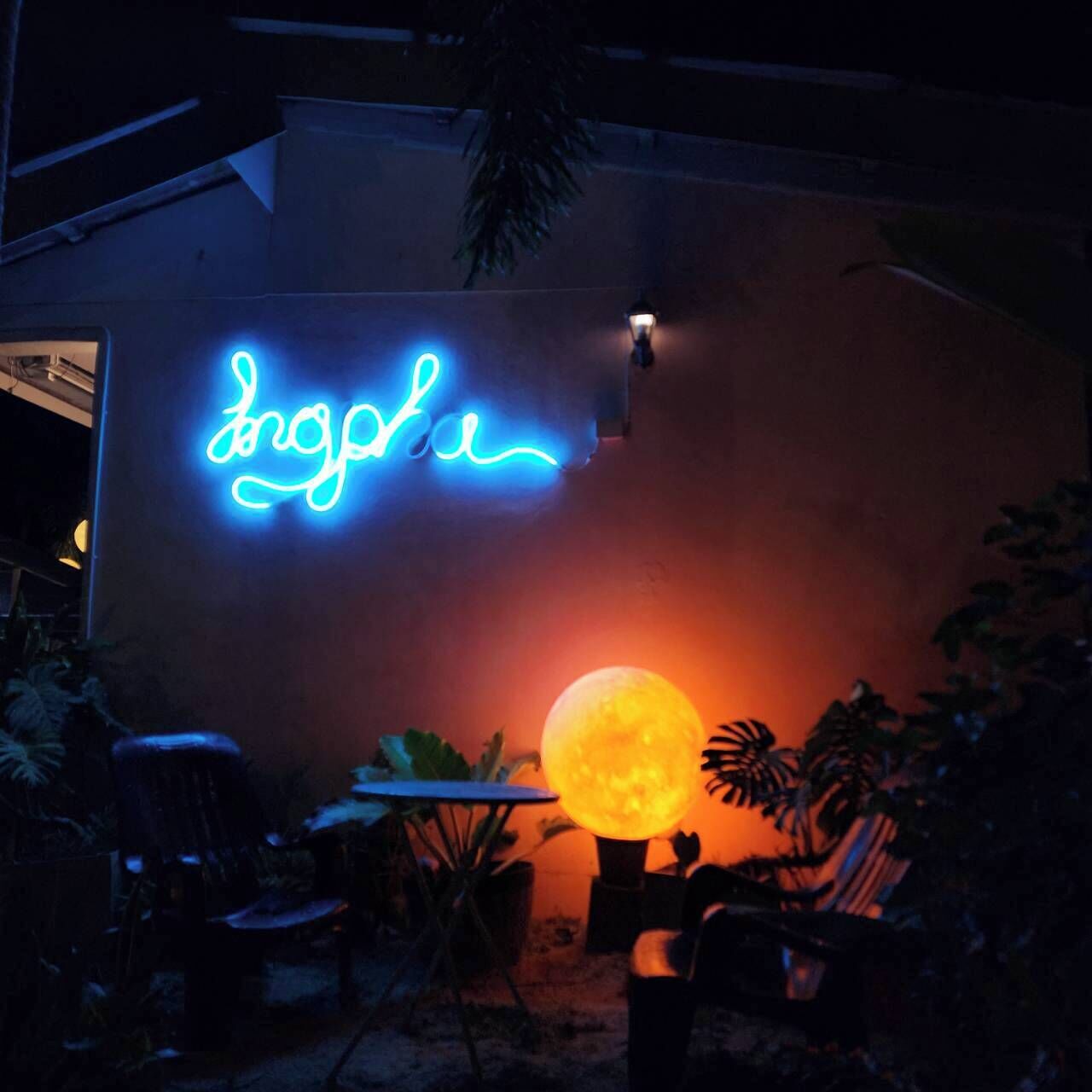 A neon sign with the word 'Dolph' on a building, a large illuminated moon sculpture, and outdoor seating with plants.