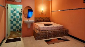 A small, orange-walled room with a bed, a sink, and a shower.