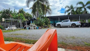 A covered outdoor area with a concrete floor, a white pickup truck, and a white building in the background.