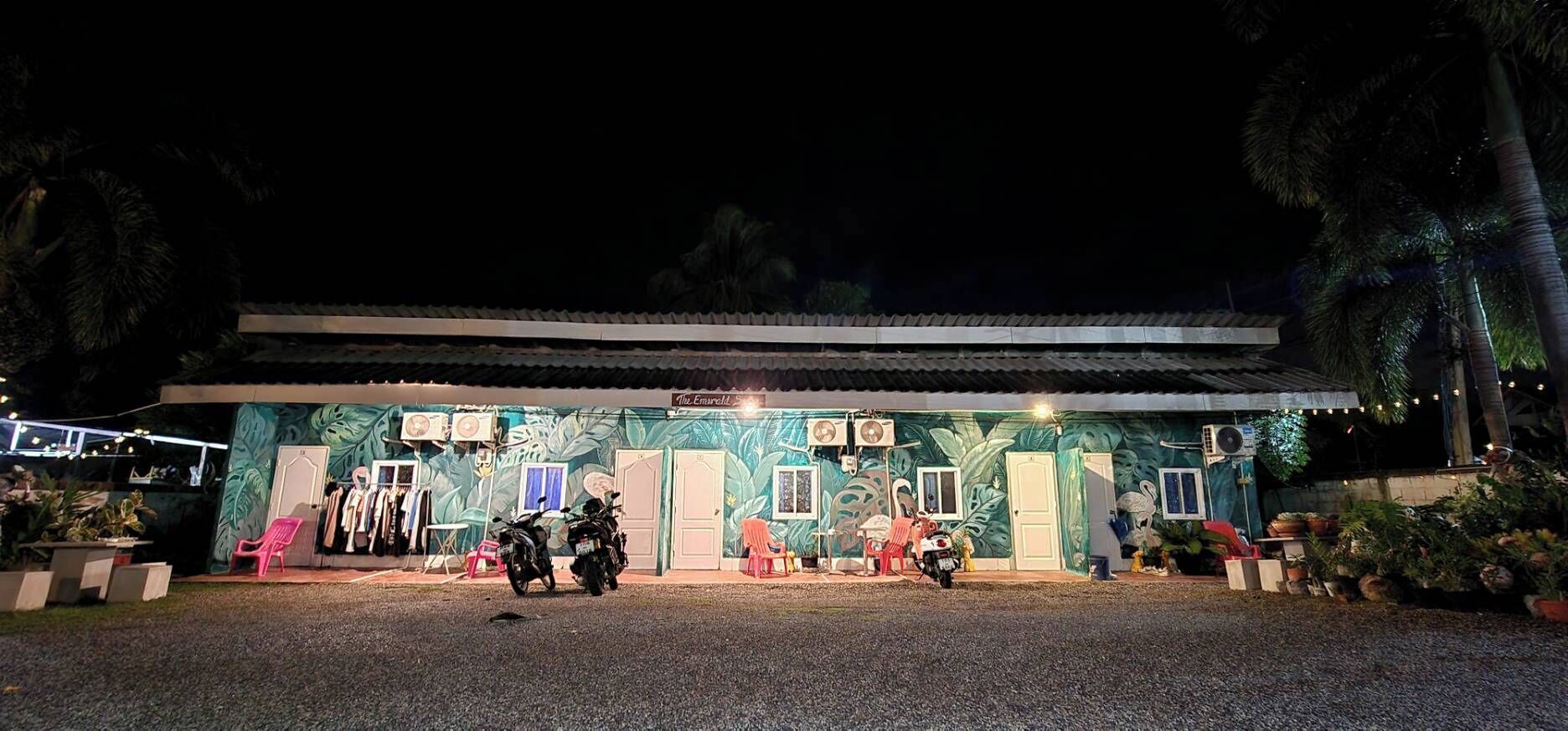 Un edificio con un mural tropical, mesas al aire libre y motocicletas estacionadas.