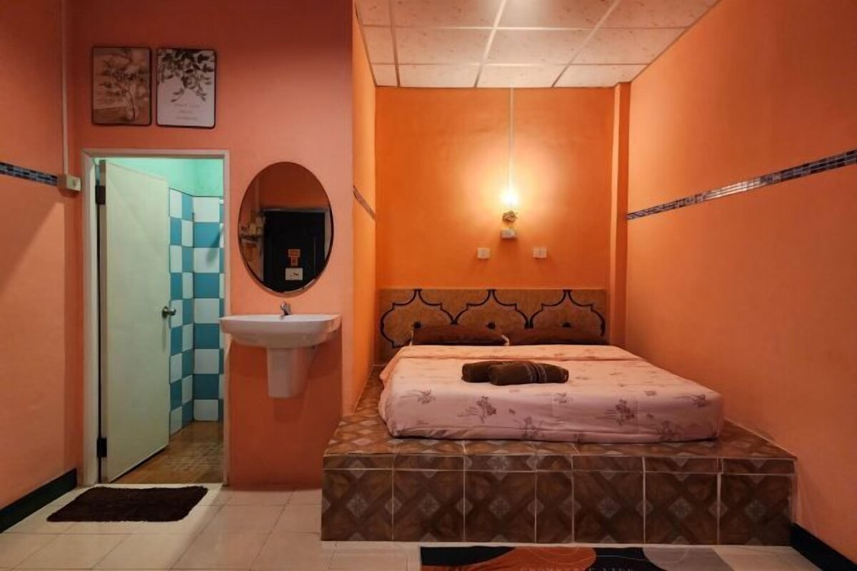 A small, orange-walled bedroom with a bed, a sink, and a mirror.