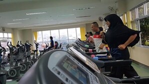 A gym with treadmills and stationary bikes, large windows, and a view of buildings outside.
