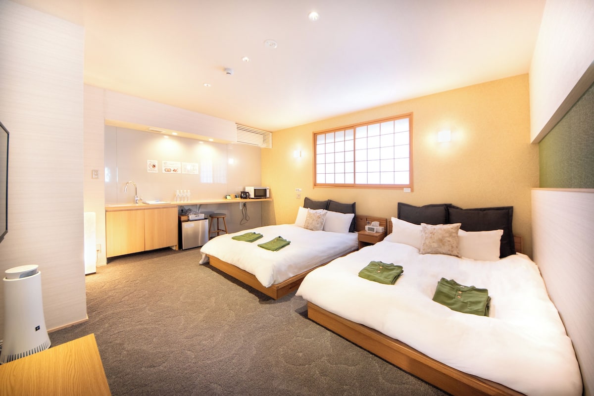 Habitación de hotel con dos camas, kitchenette y un ventanal grande.