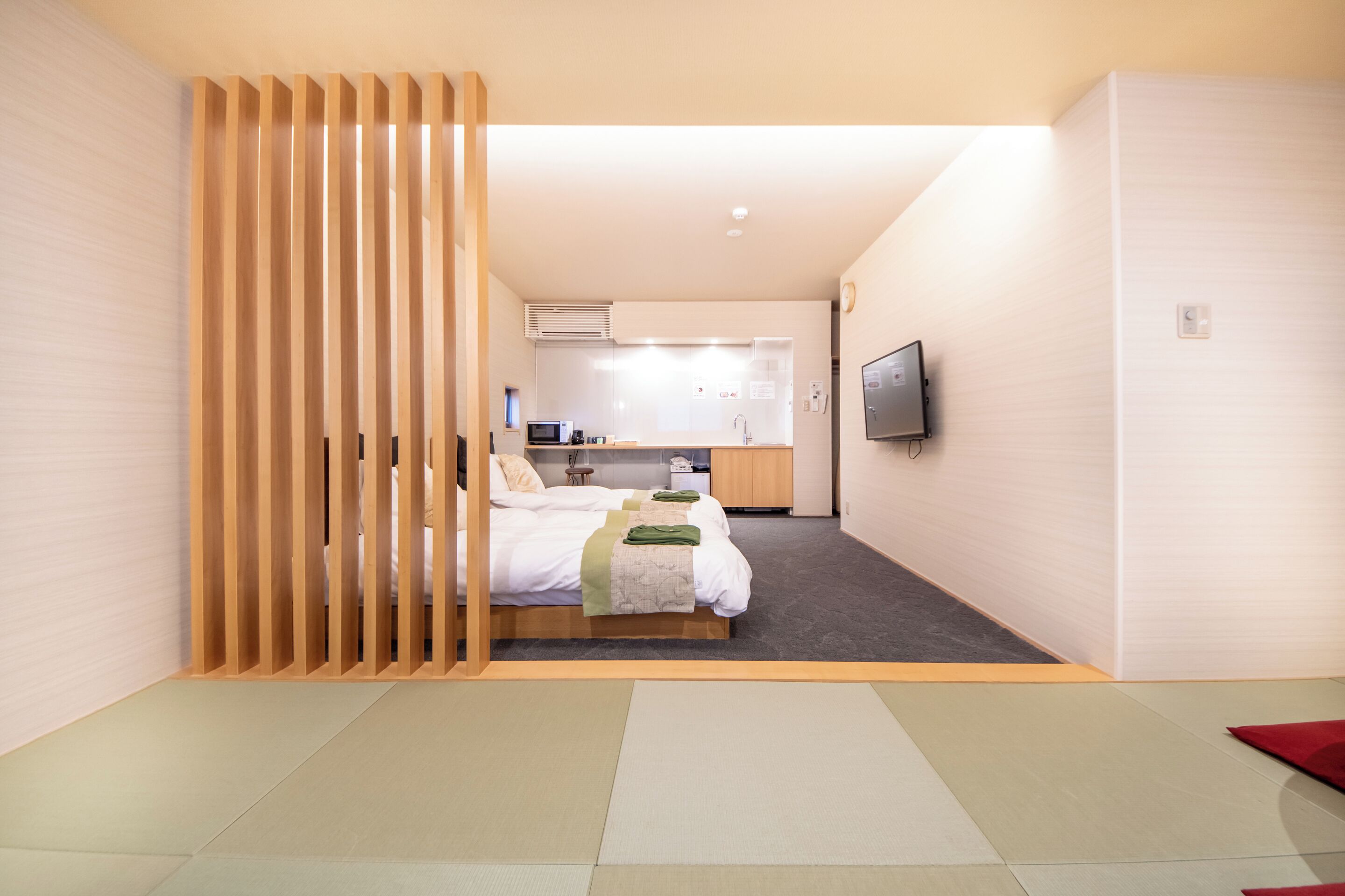 A modern hotel room with a bed, a kitchenette, and a TV.