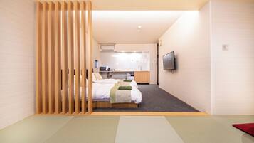 A modern hotel room with a bed, a kitchenette, and a TV.