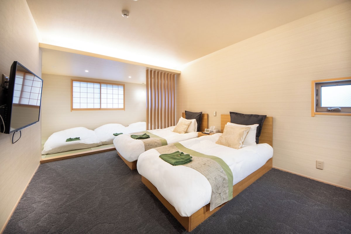 Una habitación de hotel con dos camas, televisión, ventana y puerta corredera.