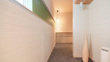 A narrow hallway with a carpeted floor, a wooden floorboard on the left, and a white trash bin on the right.