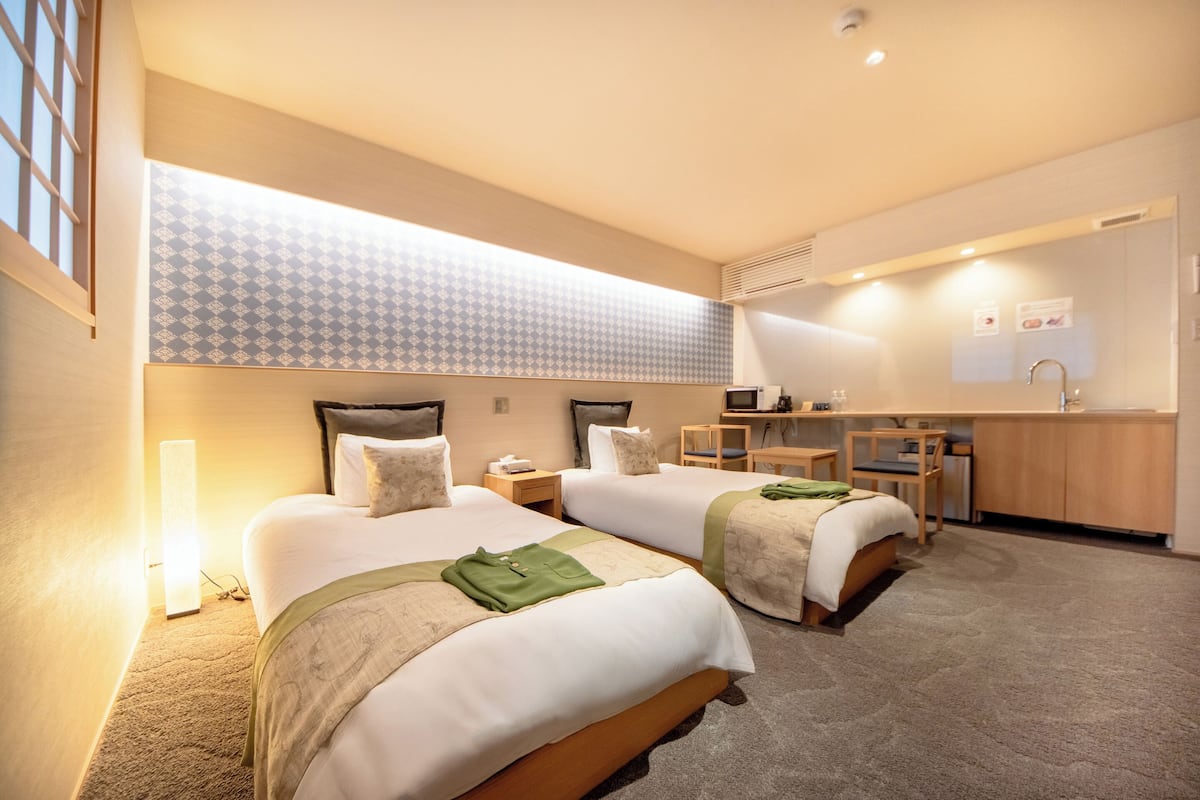 Habitación de hotel con dos camas, un escritorio y una kitchenette.