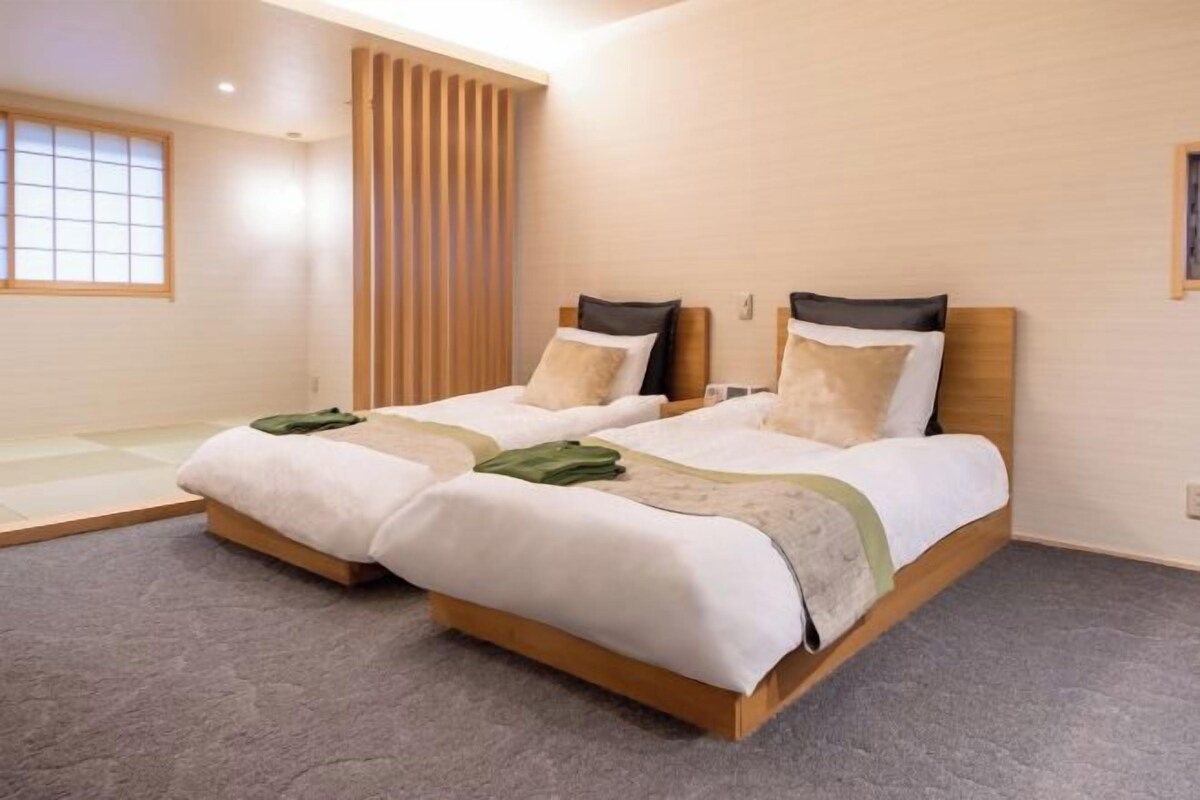 Habitación de hotel con dos camas individuales, cabecero de madera, un ventanal grande y suelo alfombrado.