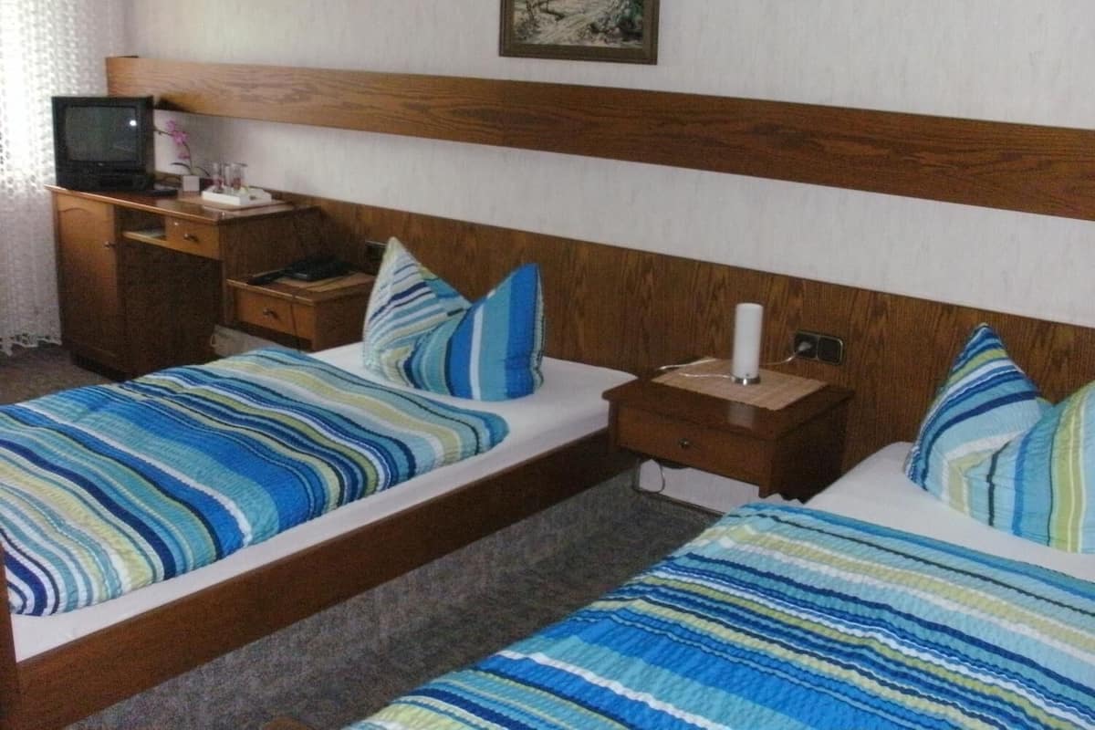 A hotel room with two beds, wooden headboard, a small desk with a lamp, and a television on a nightstand.