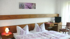 A hotel room with a wooden headboard, a bed with a purple and white striped bedspread, a desk with a computer and a lamp, and a chair. - Tannenhof (Erlenbach am Main)