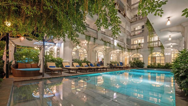 Una piscina interior con sillones de descanso y un área de estar techada, rodeada de balcones y follaje.