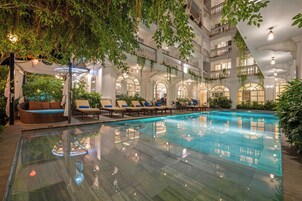 Una piscina interior con sillones de descanso y un área de estar techada, rodeada de balcones y follaje.