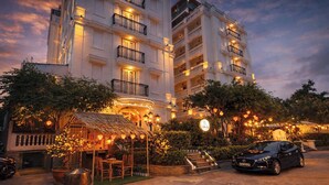 Un hotel de varios pisos con balcones y zonas de estar al aire libre, rodeado de árboles e iluminación decorativa.