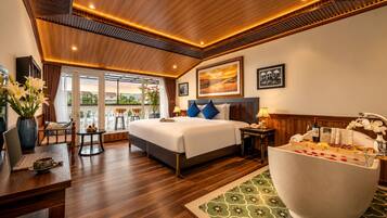 Habitación de hotel con una cama grande, zona de estar con vistas y una bañera.
