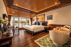 A hotel room with a large bed, a sitting area with a view, and a bathtub.