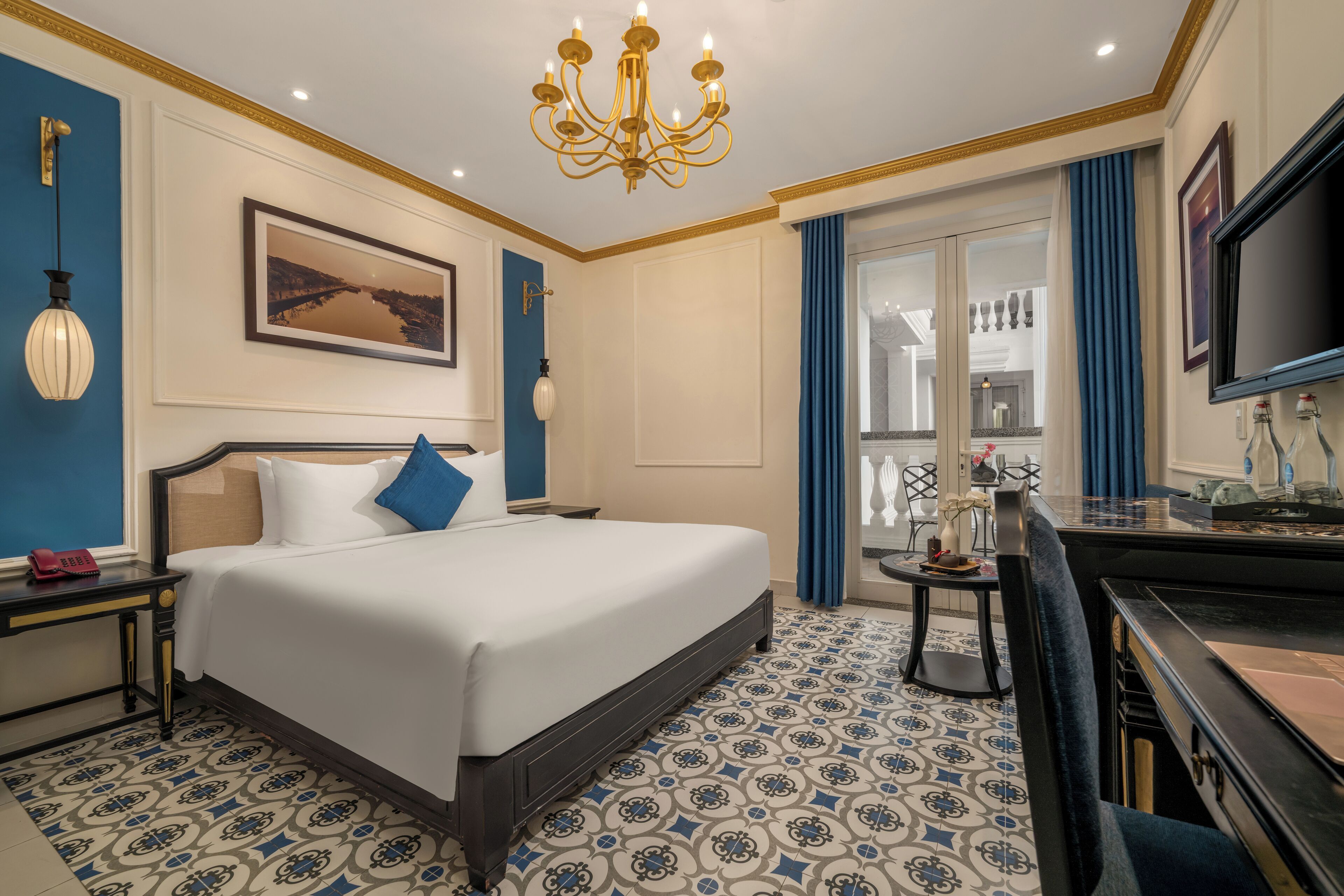 Habitació d'hotel amb un llit gran, un escriptori, una làmpada de cristall i vista a la ciutat.