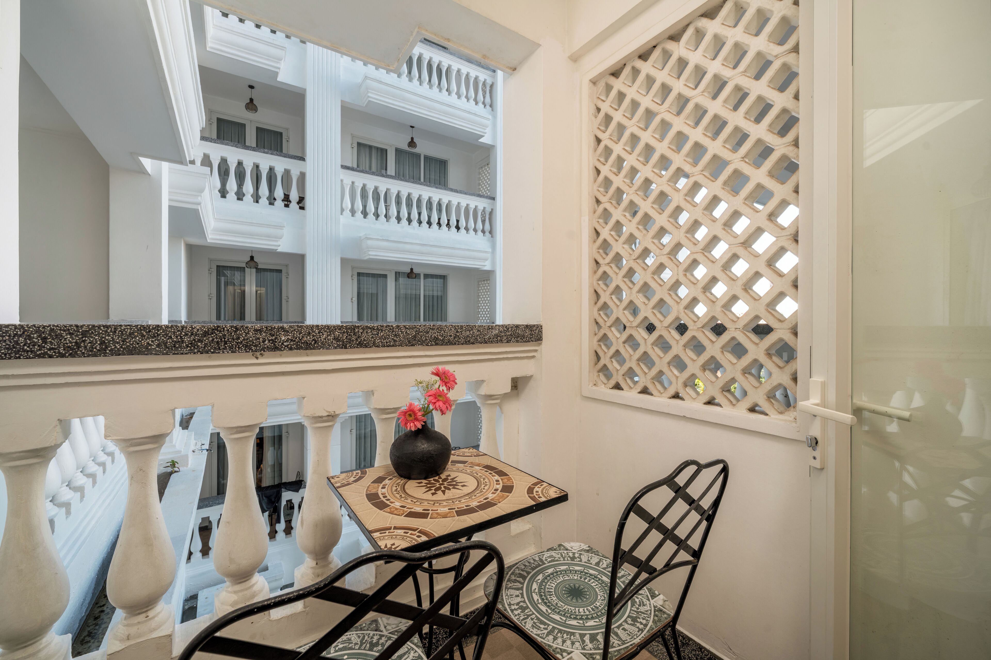 Un balcon avec une table, des chaises et un vase de fleurs.