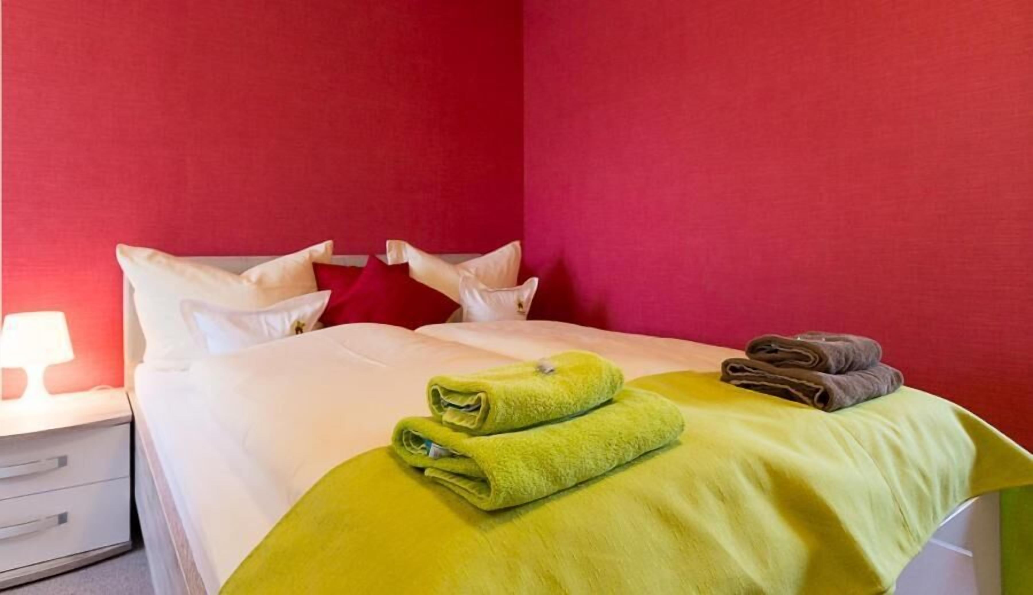 A hotel room with a bed, pillows, a nightstand, and a lamp.