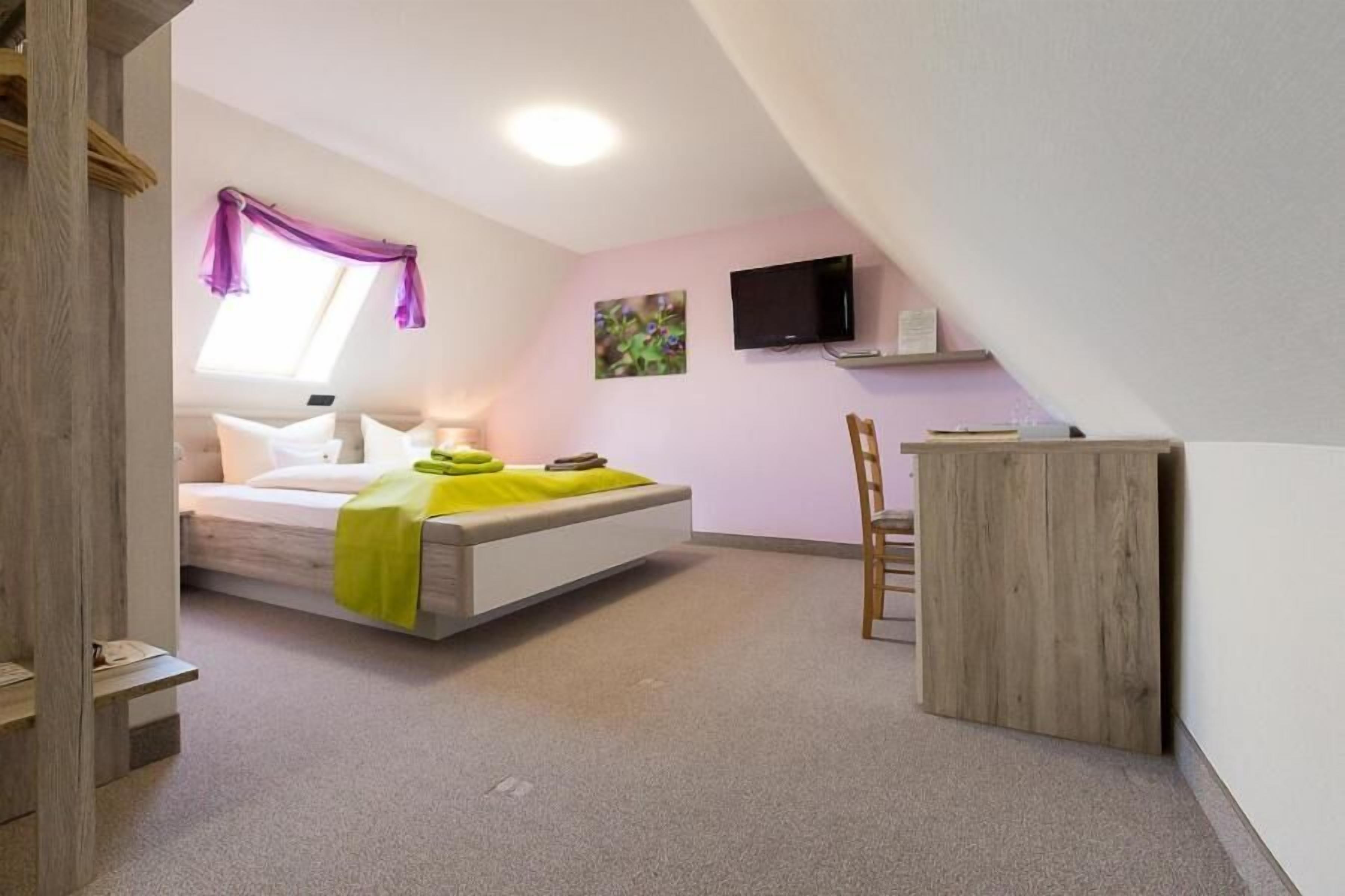 Een slaapkamer met een bed, een bureau, een stoel, een televisie en een raam met gordijnen.