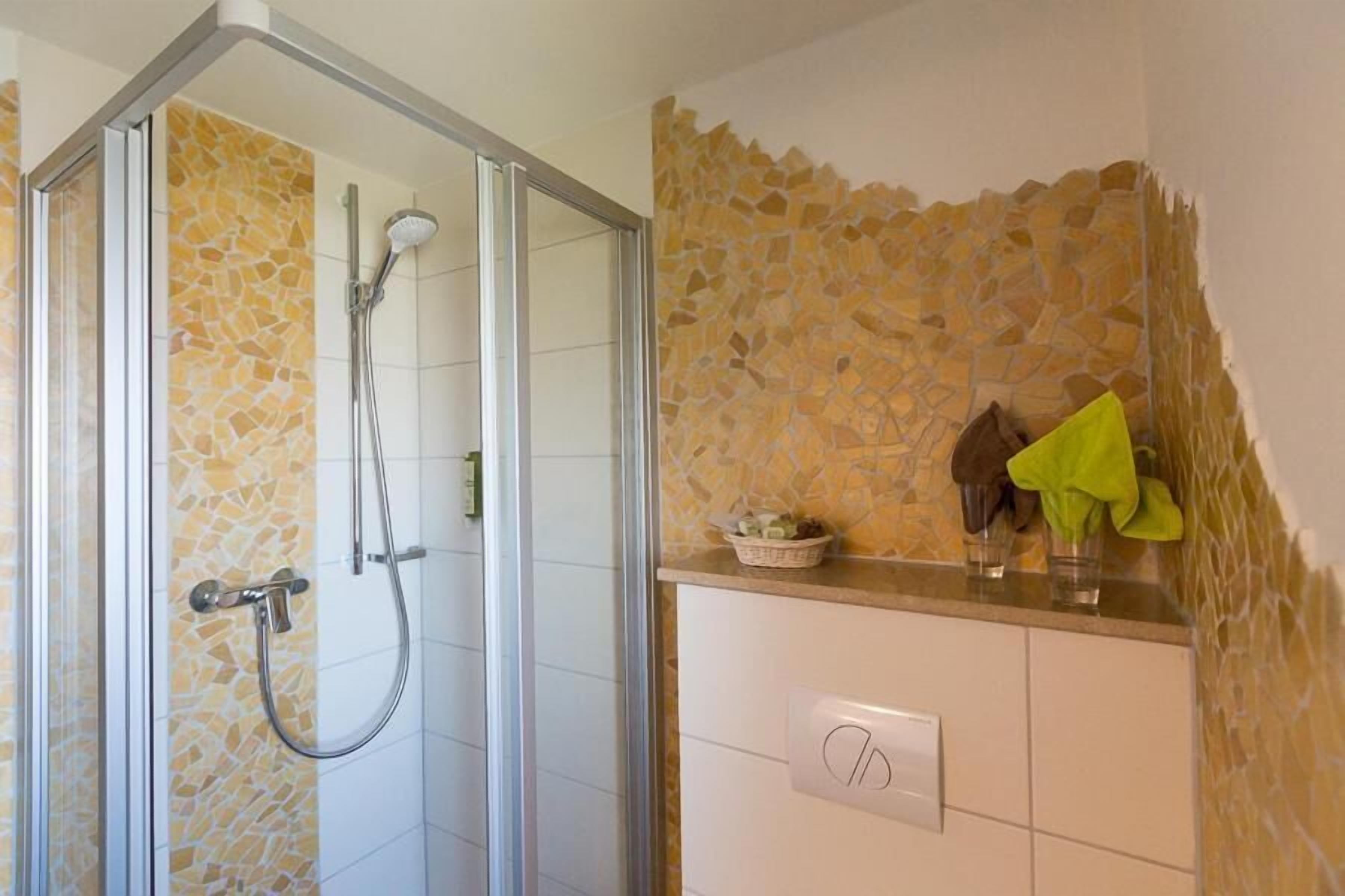 Un baño con ducha, pared de mosaico y toallero con toallas.