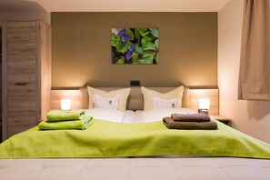 A hotel room with a large bed, two bedside lamps, a green towel, and a wall-mounted picture of flowers. - Kräuterhotel Garni zur Klostergrotte (Grammetal)