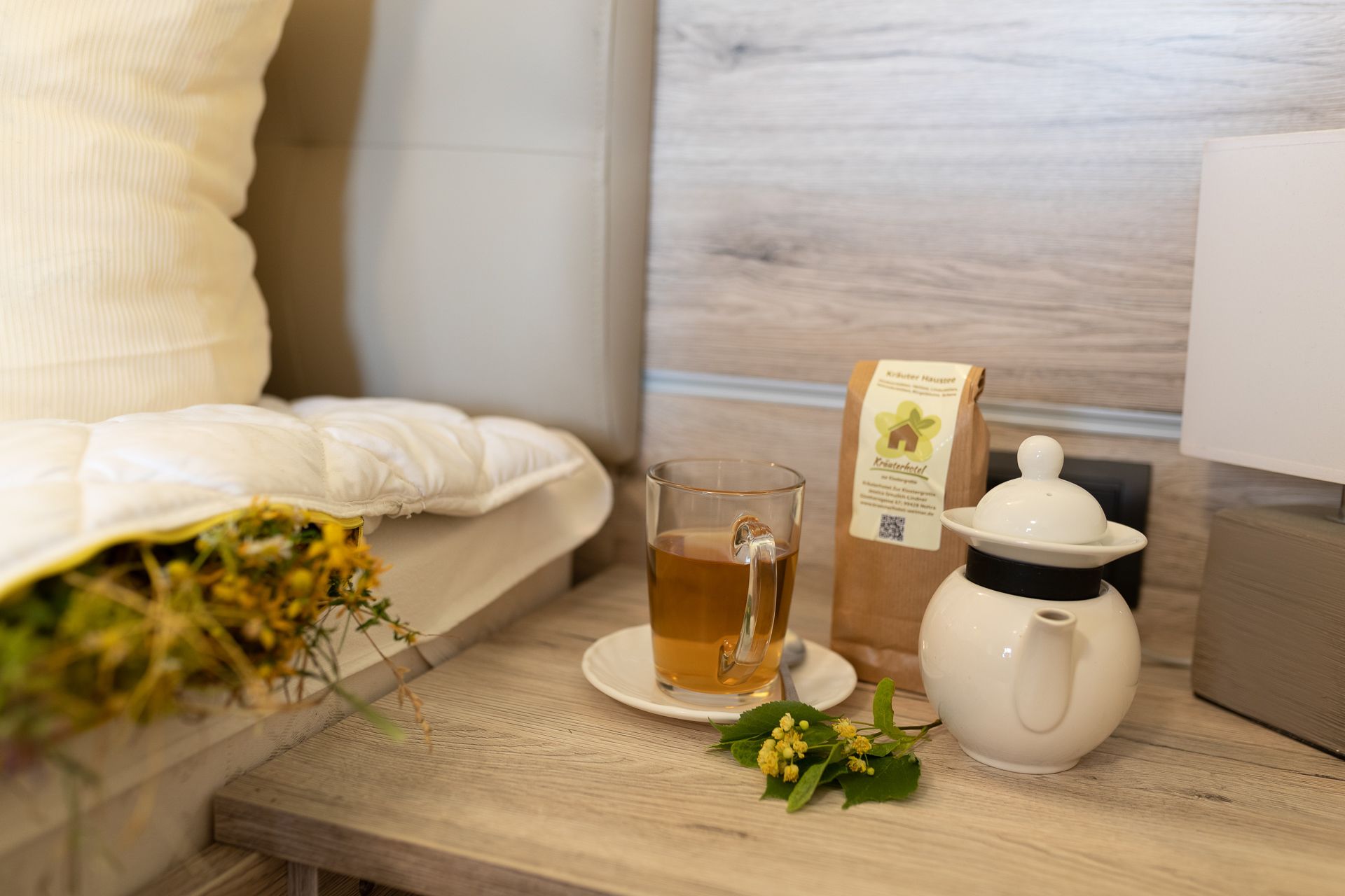 Une table en bois avec une tasse de thé, une théière, une boîte de thé et un coussin.