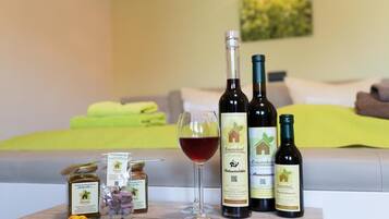Una habitación de hotel con una cama, una copa de vino tinto y tres botellas de vino sobre una mesa. También hay dos tarros de mermelada y una flor en la mesa.