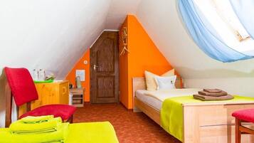 A small, cozy room with a sloped ceiling, a wooden door, a bed with a green bedspread, a small table, and a chair.