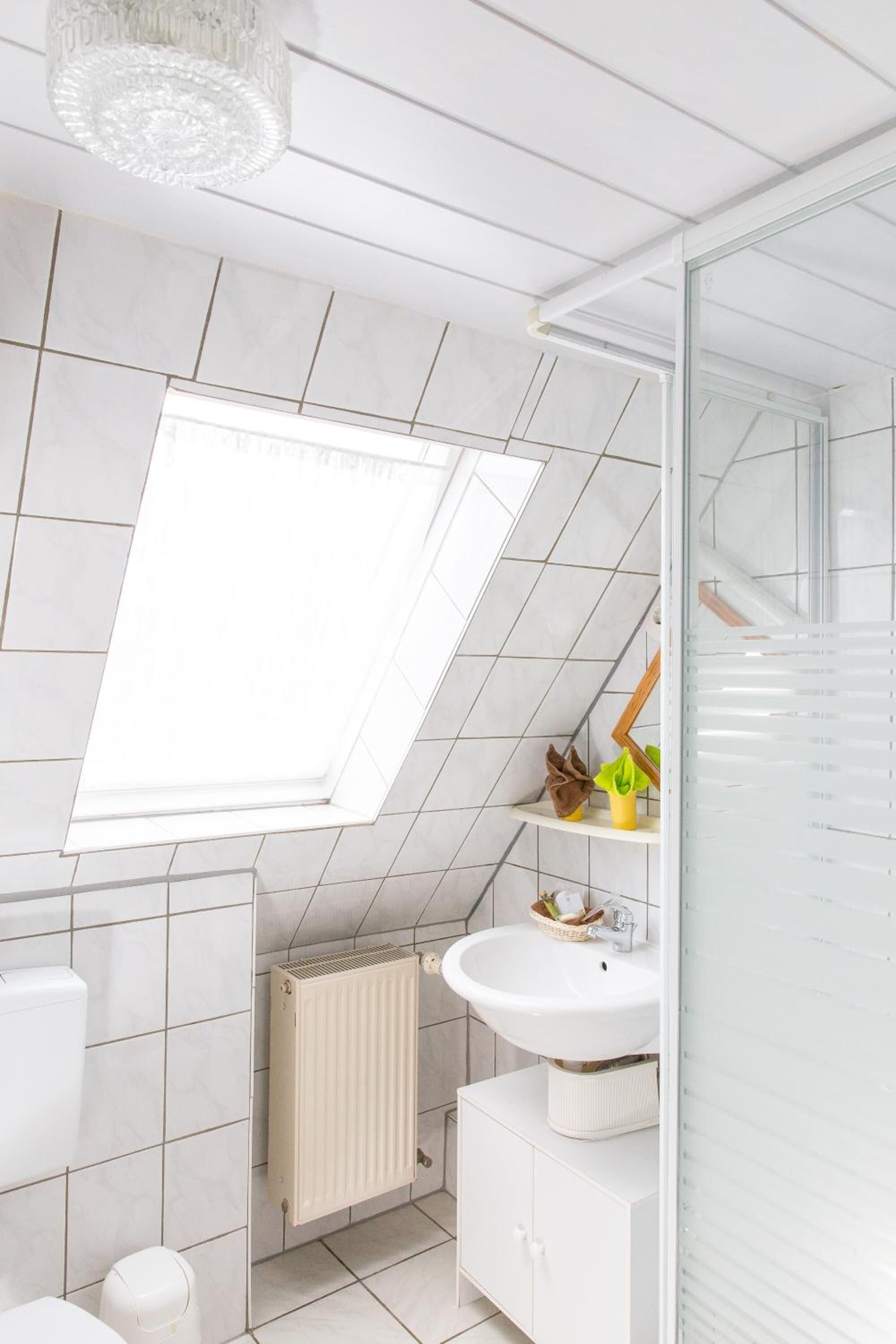 A modern bathroom with a skylight, white tiles, a radiator, a sink, and a mirror.