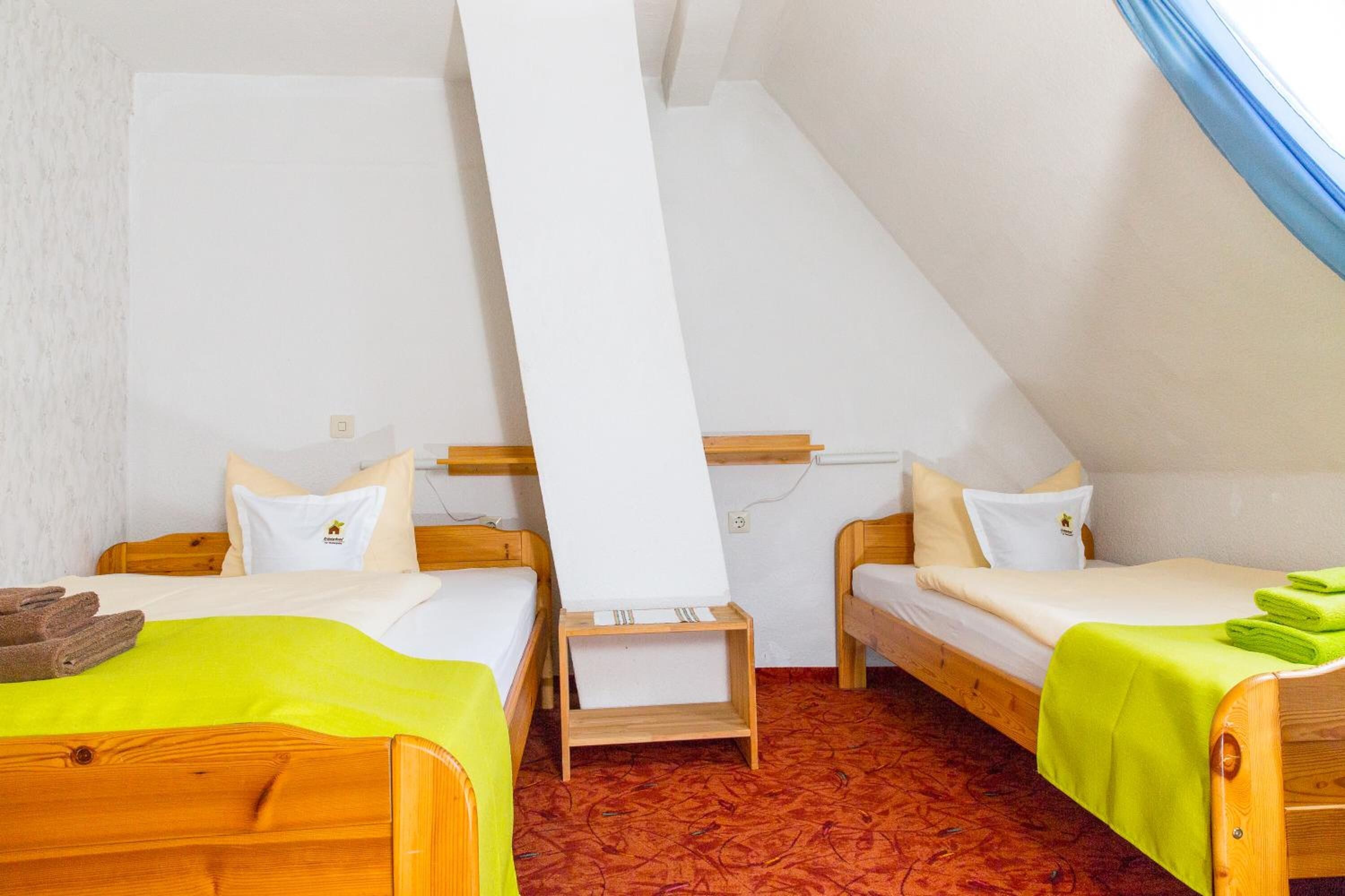 Una habitación pequeña y acogedora con dos camas de madera, una mesita y una ventana con cortinas azules.