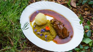 Un plato blanco con salsa verde, un elemento amarillo y uno marrón, rodeado de follaje.
