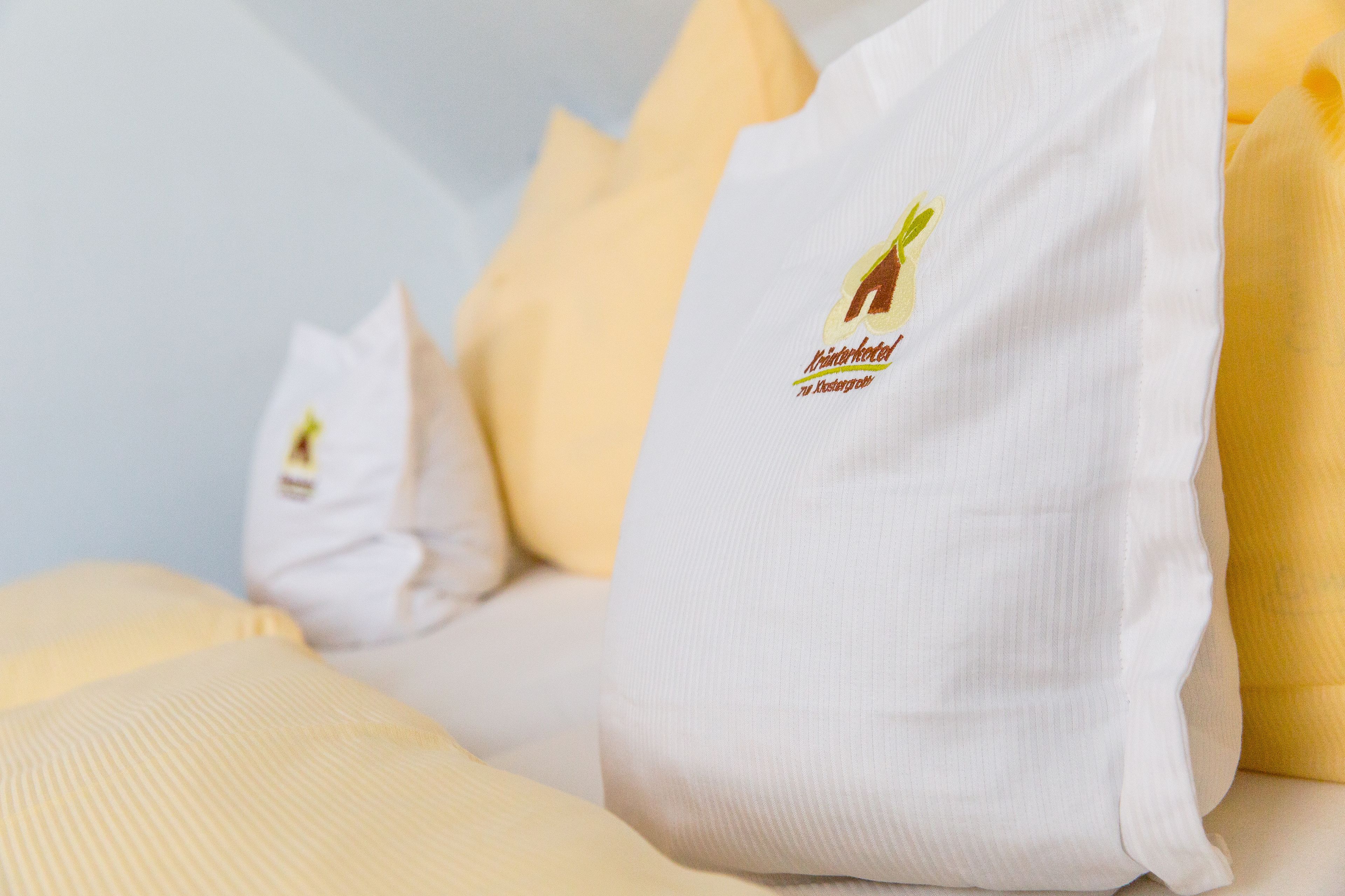 Ein Bett mit weißen Kissen, einem Logo und Text, sowie einem gelben Kopfteil.