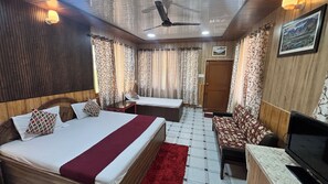 A room with a bed, a sofa, a TV, a ceiling fan, and curtains. - Hotel Ekant Lodge (Dharamshala)