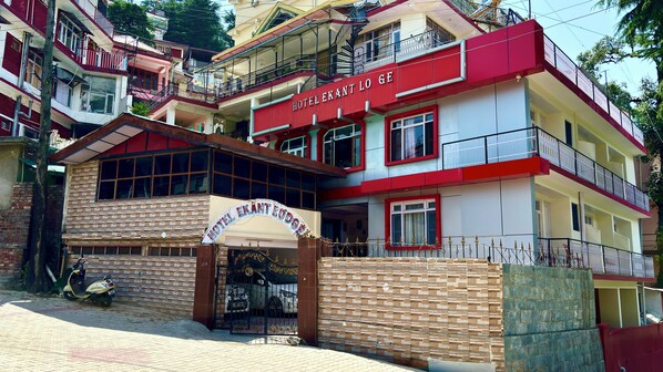 A multi-story hotel with a red and white facade, a gated entrance, and a brick facade. - Hotel Ekant Lodge (Dharamshala)